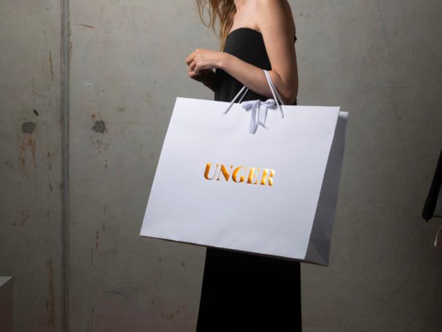 Kvinde holder en UNCLR-taske i hvid farve med gylden tekst.